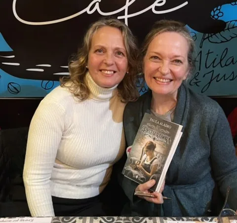 Paula Alaimo junto a una lectora que sostiene un ejemplar de La Restauradora